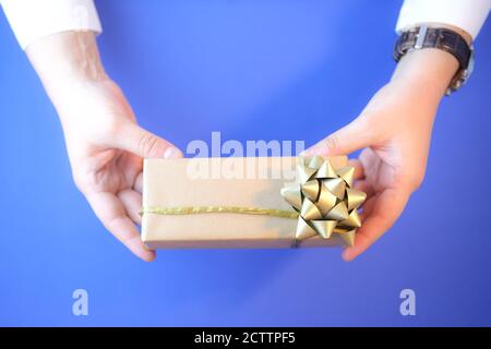 Cropped image of a man holding a gift box wrapped in craft paper. Stock Photo