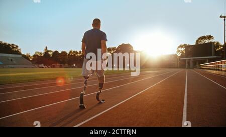 Athletic Disabled Fit Man with Prosthetic Running Blades is Walking During a Training on an Outdoor Stadium on a Sunny Afternoon. Amputee Runner Stock Photo