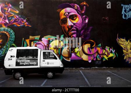 Colourful large graffiti street art on wall showing face and signatures. There is a small truck van incoungrously in the foreground Stock Photo