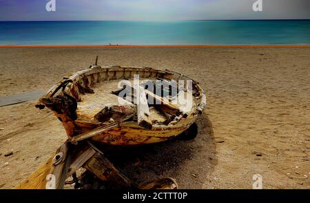 old wrecked wooden fishing boat on sandy shore showing broken machinery and sea and sky in background Stock Photo