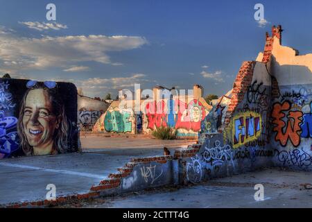Colorful large graffiti street art on abandoned factory wall showing names, faces and signatures. There is good foreground and background , blue sky Stock Photo