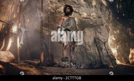 Primeval Caveman Wearing Animal Skin Holds Stone Tipped Hammer Looks Around Prehistoric Forest, Ready to Hunt Animal Prey. Neanderthal Going Hunting Stock Photo