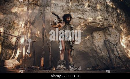 Primeval Caveman Wearing Animal Skin Holds Stone Tipped Hammer Looks Around Prehistoric Forest, Ready to Hunt Animal Prey. Neanderthal Going Hunting Stock Photo