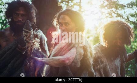 Female Leader and Two Primeval Cavemen Warriors Threat Enemy with Stone Tipped Spear, Scream, Defending Their Cave and Territory in the Prehistoric Stock Photo