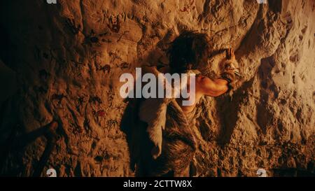 Primitive Prehistoric Neanderthal Wearing Animal Skin Draws Animals and Abstracts on the Walls at Night. Creating First Cave Art with Petroglyphs Stock Photo