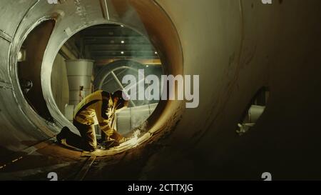 Professional Heavy Industry Welder Working Inside Pipe, Wears Helmet and Starts Welding. Construction of the Oil, Natural Gas and Fuels Transport Stock Photo