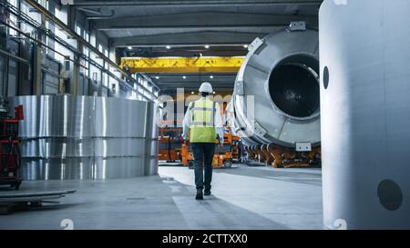 Following Shot of Heavy Industry Engineers Walking Through Manufacturing Factory. In the Background Professionals Working on Construction of Oil, Gas Stock Photo