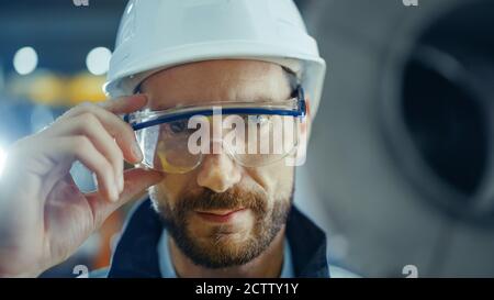 Portrait of Smiling Professional Heavy Industry Engineer Worker Wearing Safety Uniform, Goggles and Hard Hat. In the Background Unfocused Large Stock Photo