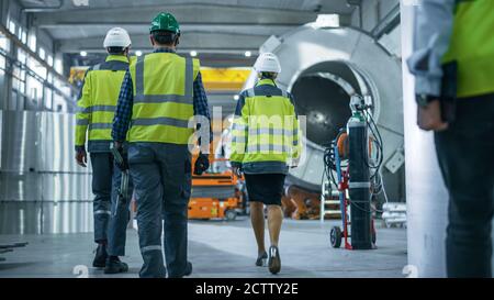 Shot of Heavy Industry Engineers and Workers Walking through Pipe Manufacturing Factory. Modern Facility for Design and Construction of Oil, Gas and Stock Photo