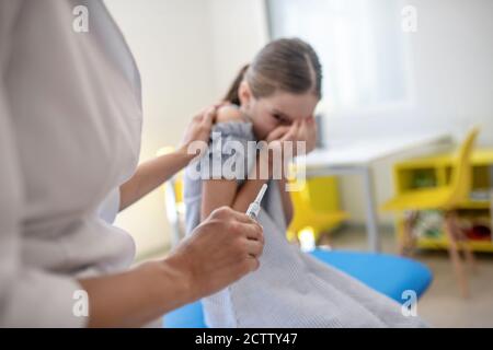 Girl looking at the syring in doctors hand and feeling scared Stock Photo