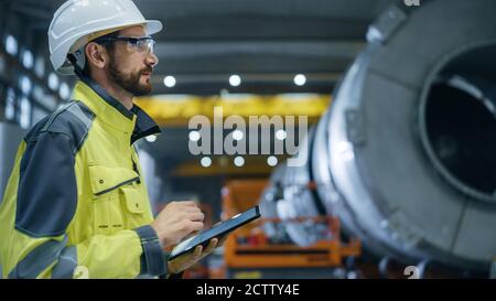 Heavy Industry Engineer in Pipe Manufacturing Factory, Use Digital Tablet Computer. Facility for Construction of Oil, Gas and Fuel Pipeline Stock Photo