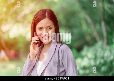 Asian business woman using phone calling at park with green outdoors background. Stock Photo