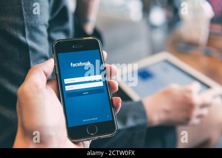 Facebook App login page on iPhone with people using tablet background for social network security on mobile smartphone.,20 July 2019,Bangkok, THAILAND Stock Photo