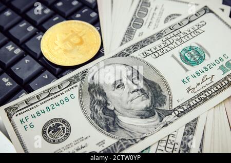 bitcoin coin is lying on the keyboard of a laptop with a bundle of USA dollars in close-up. Concept of business and Commerce. Stock Photo