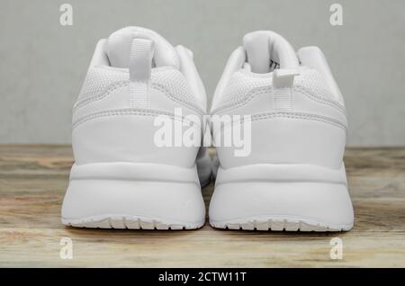 Beautiful pair of new white women's sneakers on a wooden background close up. Heel part of sneakers close up Stock Photo