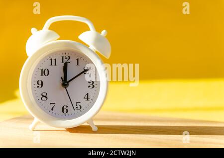 White alarm clock stands on a wooden table on a yellowbackground in the sunlight, copy space Stock Photo