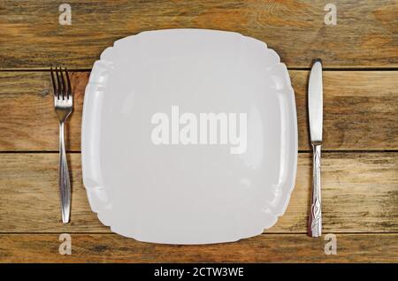 Empty white plate, knife, fork on a wooden background, top view, copy space Stock Photo