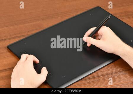 Hand of the designer with a pen on a tablet. Isolated on wood background. High resolution photo. Full depth of field. Stock Photo