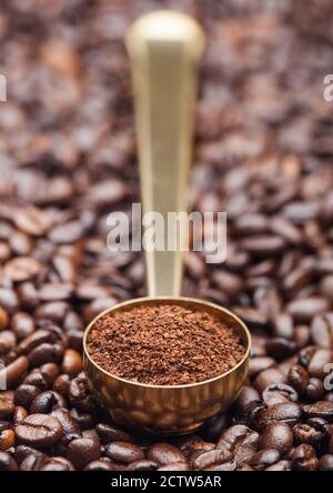 Ground coffee in golden steel scoop on fresh coffee beans background. Macro Stock Photo