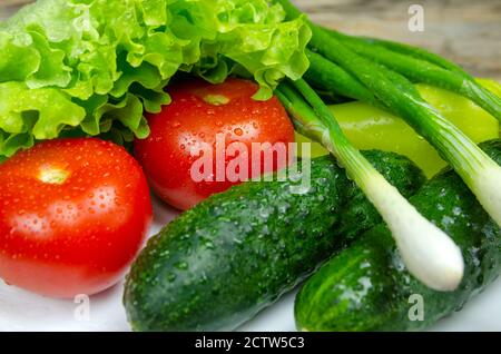 beautiful fresh, juicy vegetables with drops of water on a white plate: fresh peppers, tomatoes, cucumbers, lettuce, dill, green onions Stock Photo