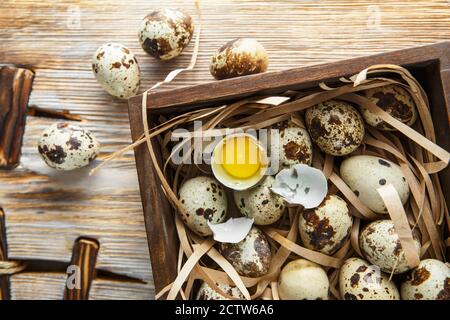 Quail eggs. Flat lay composition with small quail eggs in the wooden box on the natural wooden background. Two broken eggs with a bright yolk. Quail e Stock Photo