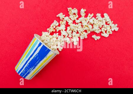 Spilled popcorn from a paper Cup on a red background, top view, copy space. Stock Photo