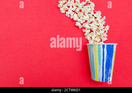 Spilled popcorn from a paper Cup on a red background, top view, copy space. Stock Photo