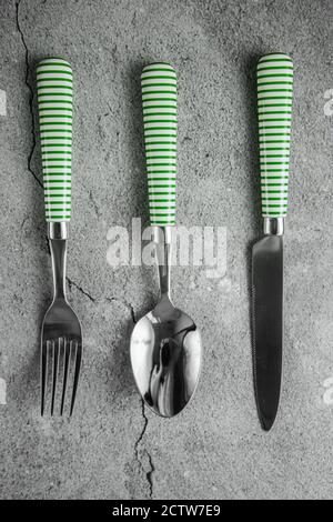 Cutlery on gray concrete background. Spoon, fork, knife with white and green stripes on handles Stock Photo