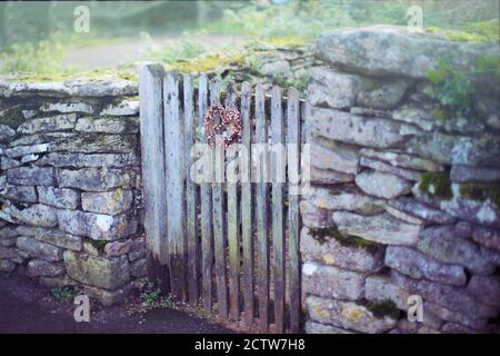 Old English dry stone wall with a nostalgic christmas dried twig wreath hanging on wooden gate. Holiday homecoming concept. Stock Photo