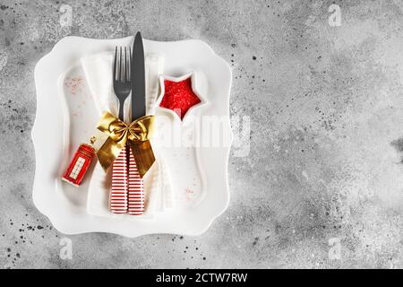 Christmas table place setting with square plate, cutlery with festive decorations gold ribbon, bauble red telephone box, star-shaped bowl with red sug Stock Photo