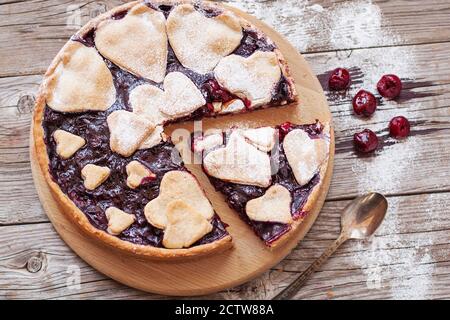 Homemade cherry pie on rustic background. Delicious homemade cake with cherries and a heart-shaped crust sprinkled with powdered sugar. Flat lay compo Stock Photo
