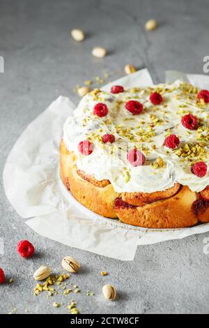 Cinnabon buns. Sinabon rolls with cream cheese, cream and brown sugar on grey background. Cinnamon rolls with raspberries and pistachios Stock Photo