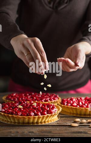 Beautiful freshly made cherry tart decorated with almond chips. Food photography. Process of making tart. Close up hands of the chef sprinkling cake w Stock Photo