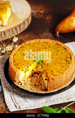 Cheese cake with passion fruit on a dark background. Cheese cake with passion fruit sauce on top, decorated with mint leaves. Stock Photo
