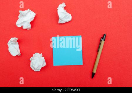 Blue sheet of paper with copy space, crumpled paper and pen on red background, top view. Stock Photo