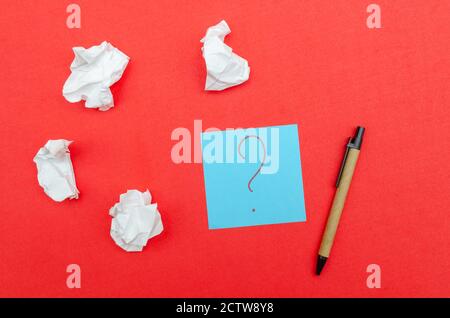 Blue sheet of paper with a question mark, crumpled paper and a pen on a red background, top view. Stock Photo