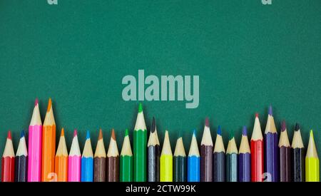 Colored pencils at the bottom on a green background with copy space, top view Stock Photo