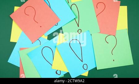 Lots of colorful note sheets with question and exclamation marks on a green background, copy space, top view Stock Photo