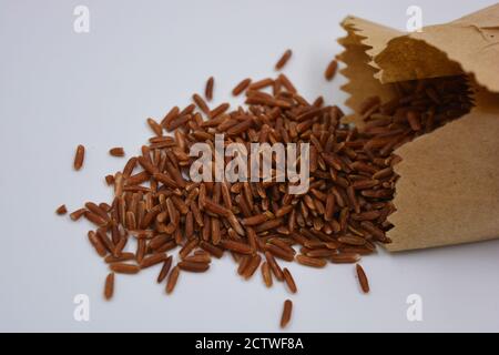 Large healthy red long rice poured out of a brown paper bag on a white background. Healthy food, healthy cereals for human life. Stock Photo