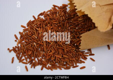 Large healthy red long rice poured out of a brown paper bag on a white background. Healthy food, healthy cereals for human life. Stock Photo