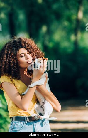 curly woman in summer outfit making duck face while holding jack russell terrier dog in park Stock Photo