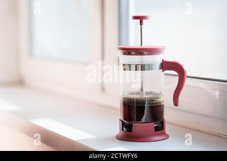 Glass Frenchpress on the windowsill in the rays of bright sunlight. The process of brewing ground black coffee. A fragrant drink made from roasted Stock Photo