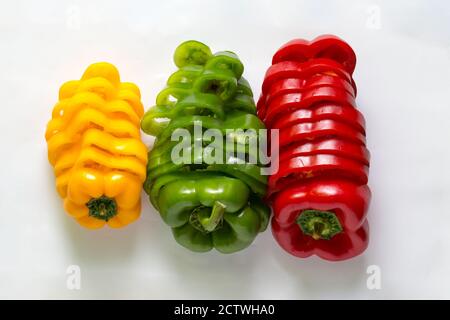 Three red, green and yellow bell peppers cut into slices on a white background Stock Photo