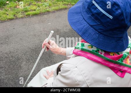 Ninety year old visually impaired lady with white stick sitting on bench in public park. England, UK Stock Photo