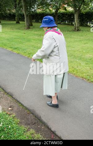 Ninety year old visually impaired lady with white stick sitting on bench in public park. England, UK Stock Photo