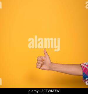 Female hand shows thumbs up in studio. Hand with yellow manicure on yellow background. Close up shot. High quality photo Stock Photo