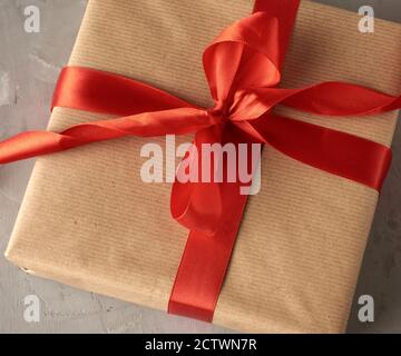 knotted bow made of red silk ribbon on brown kraft paper background, festive backdrop Stock Photo