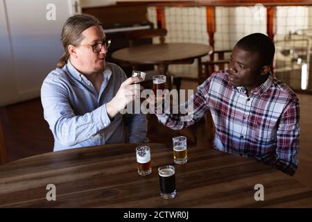 Caucasian and African American men with shirts in a microbrewery pub tasting beers and toasting Stock Photo