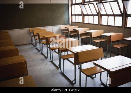 Side view of an empty classroom, with desks in formation and blackboard behind them, with open windows in sunny day Stock Photo