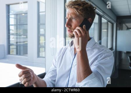 Smart casually dressed Caucasian male business creative with blonde hair and beard looking out of window, talking on smartphone. Creative business pro Stock Photo